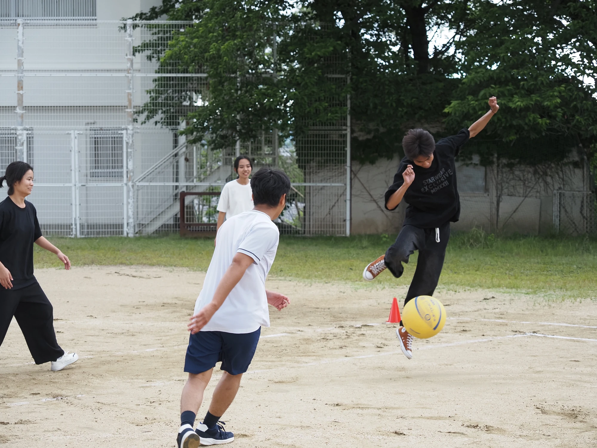 校舎を背景にボールを蹴ってスポーツを楽しむ学生たち